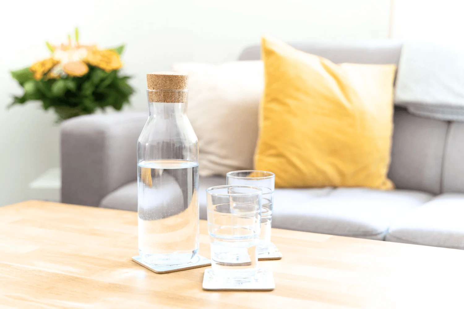 Sitzbereich im Praxisraum von BeziehungsMut in Graz mit grauem Sofa, gelbem Polster und Wasserkaraffe am Tisch